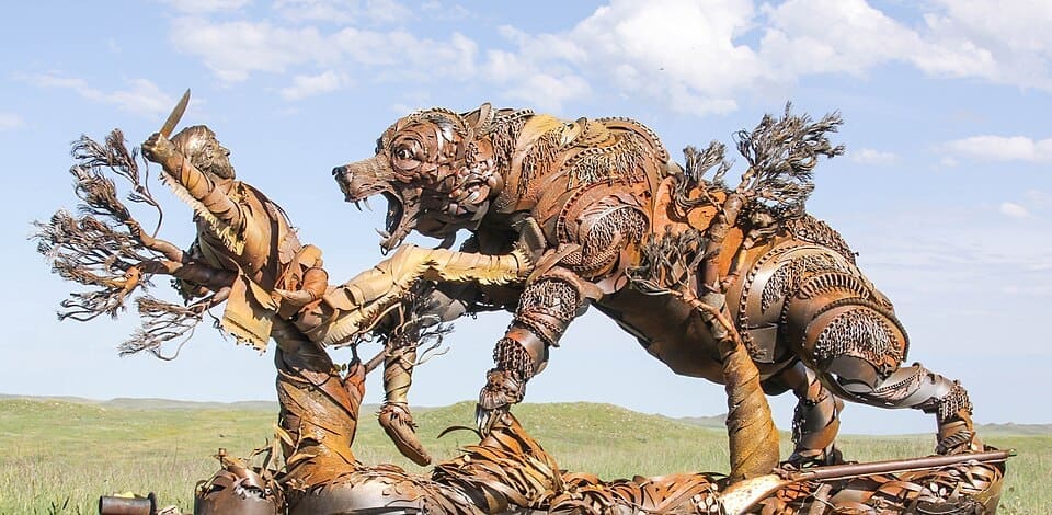 A metal sculpture of a man leant backwards defending himself with a knife against a grizzly bear.