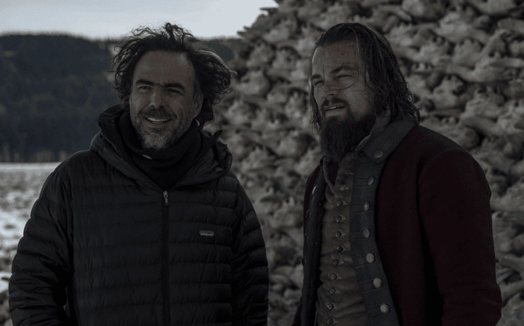 Director of The Revenant stood alongside Leonardo DiCaprio whose in full costume for his role as Hugh Glass. Behind the two are a pile of buffalo skulls with the a line of trees in the background.