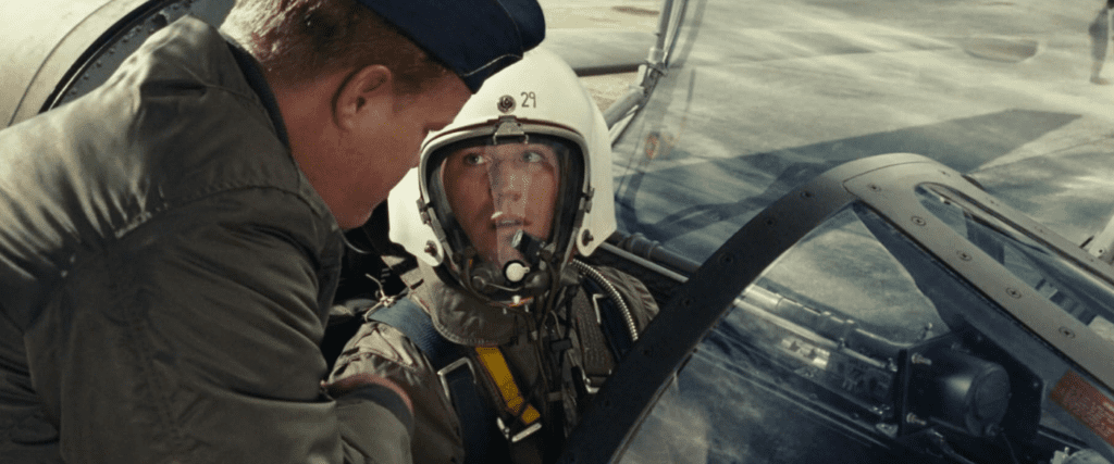 Austin Stowell as Francis 'Gary' Powers in Bridge of Spies, he's sat in the cockpit of his U-2 Spy plane in his flight suit, looking over at another man in uniform peering into the plane.