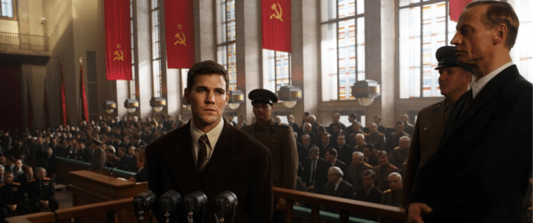 A man in a suit stands on trial, red soviet flags line the walls behind him.