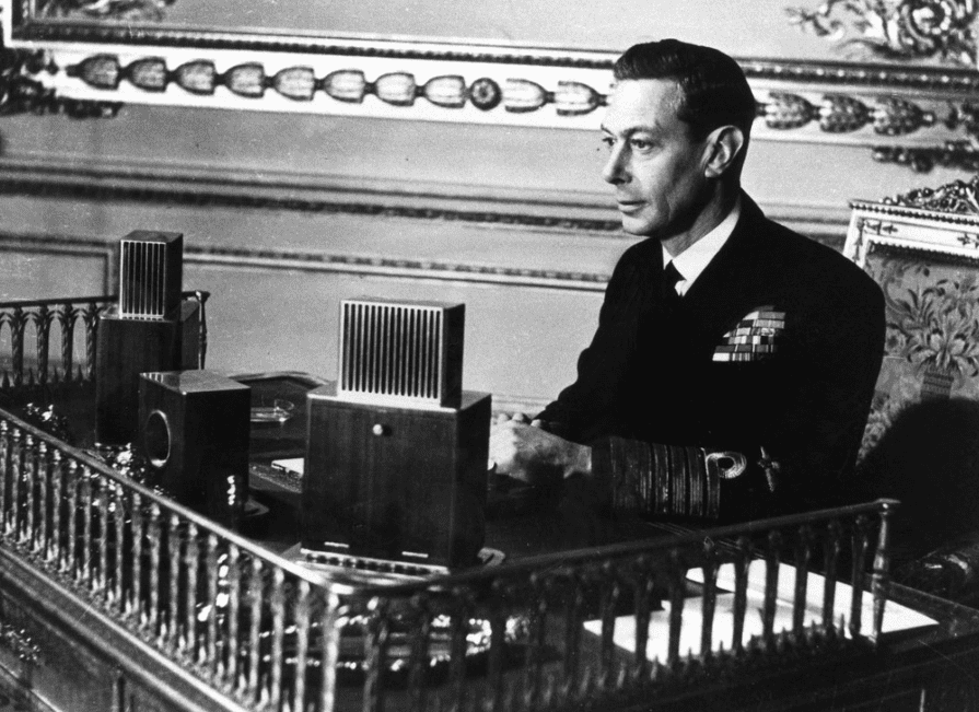 A man in a black suit sat at a desk with recording devices