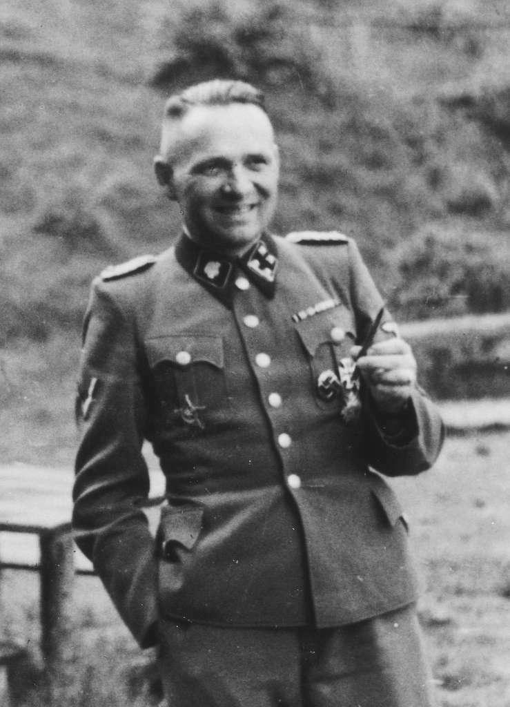 A man in nazi uniform smiles holding a type of cigarette